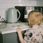 Małe dziecko sięga po jedzenie na blacie małej kuchni obok czajnika i mikrofali