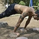 Mężczyzna trenujący podwyższone pompki na skałach w parku