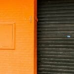 Pomarańczowa ściana z imitacją cegieł i czarną roletą w miejskiej zabudowie