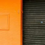 Pomarańczowa ściana z imitacją cegieł i czarną roletą w miejskiej zabudowie