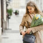 Kobieta w trenczu z tulipanami i torebką na miejskim chodniku