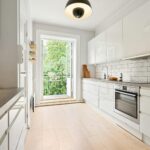Jasna nowoczesna kuchnia dwuliniowa z białymi szafkami i wyjściem na balkon