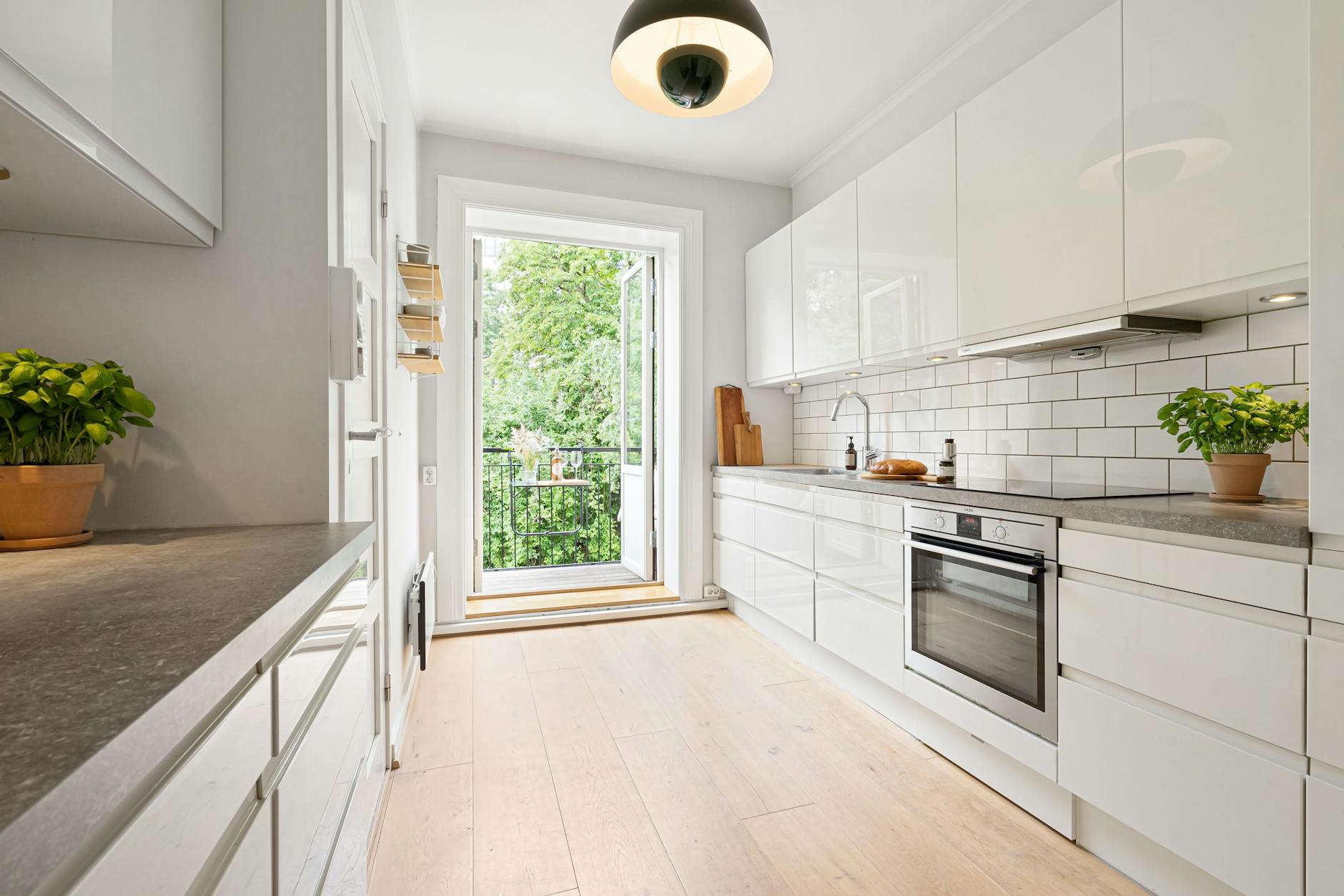 Jasna nowoczesna kuchnia dwuliniowa z białymi szafkami i wyjściem na balkon