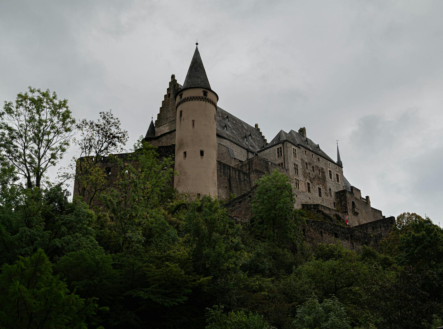 Zamek Vianden w Luksemburgu otoczony zielenią pod pochmurnym niebem