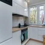 Jasna minimalistyczna kuchnia w bloku z białymi szafkami i oknem